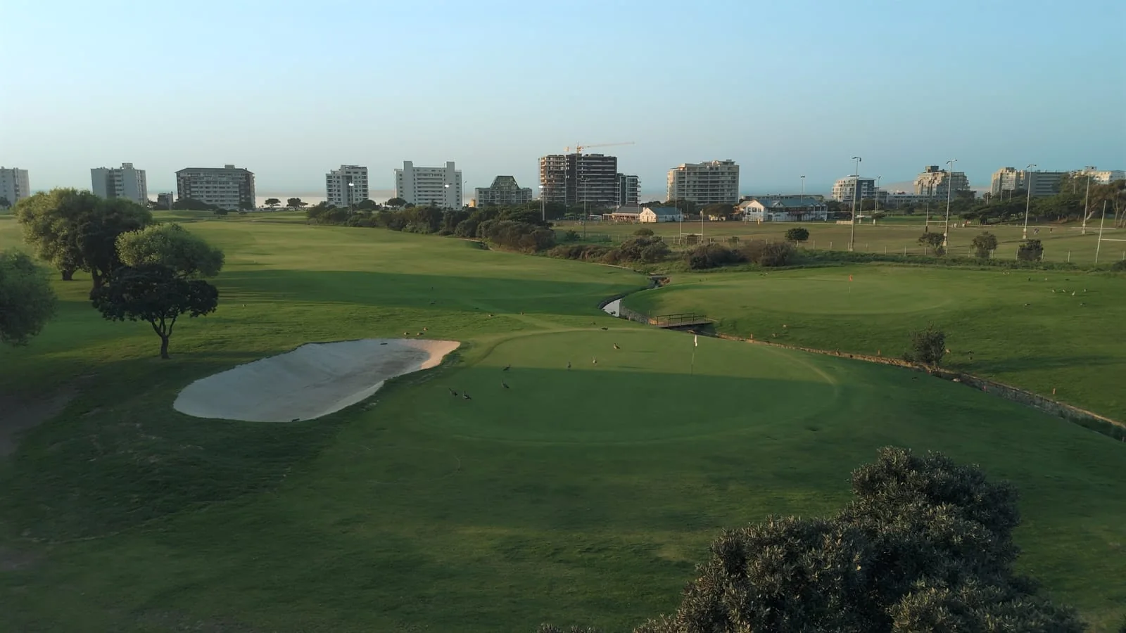 A green and bunker in low sun, with the seafront behind