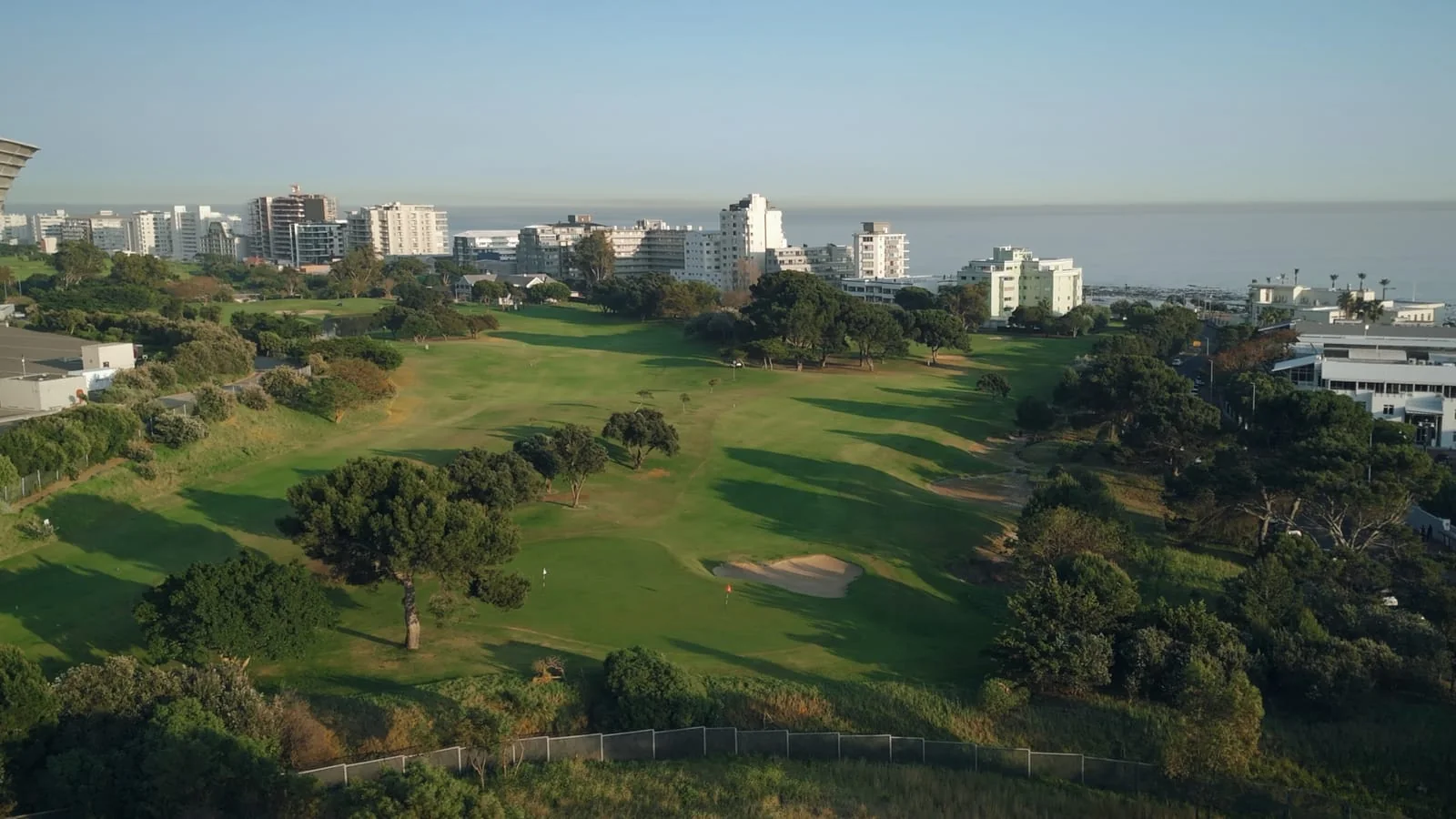 A green among the trees, with the sea behind