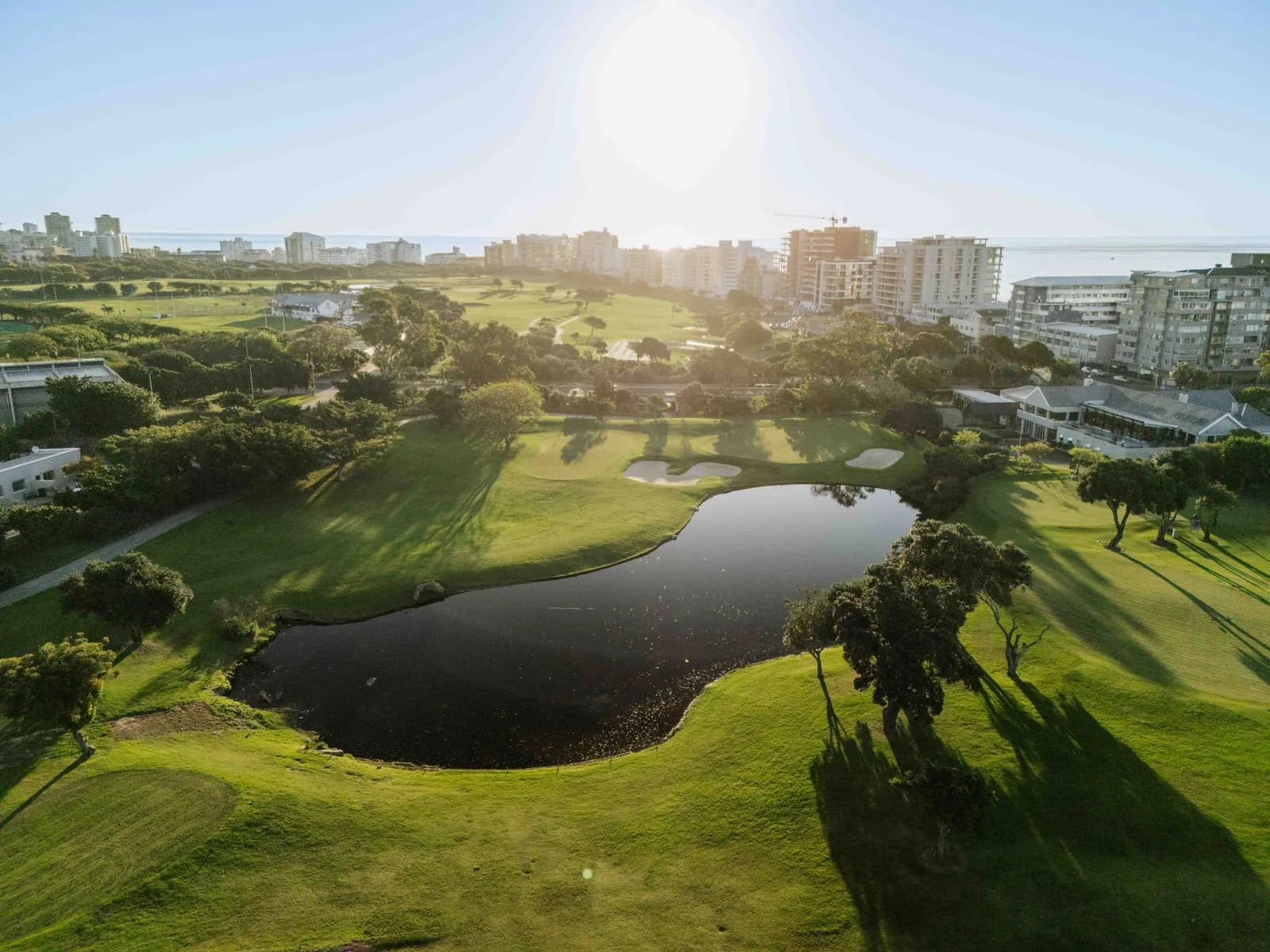 The sun over a pond and green, with the seafront apartments beyond